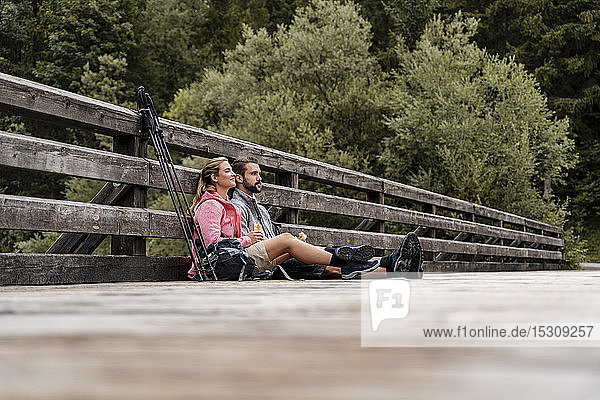 Junges Paar macht während einer Wanderung auf einer Holzbrücke eine Pause  Vorderriss  Bayern  Deutschland
