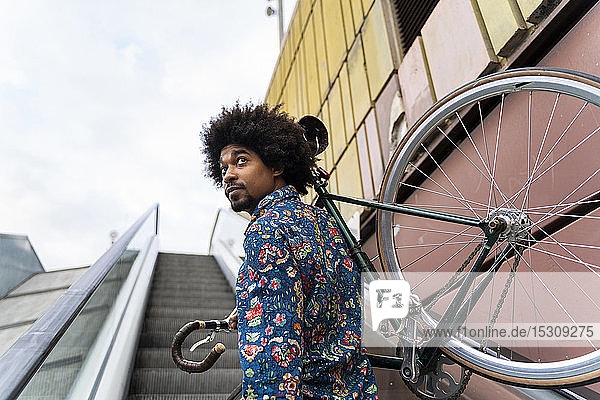 Eleganter Mann trägt Fahrrad auf Rolltreppe