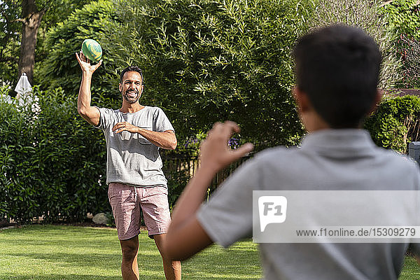Father and son playing with american football in garden