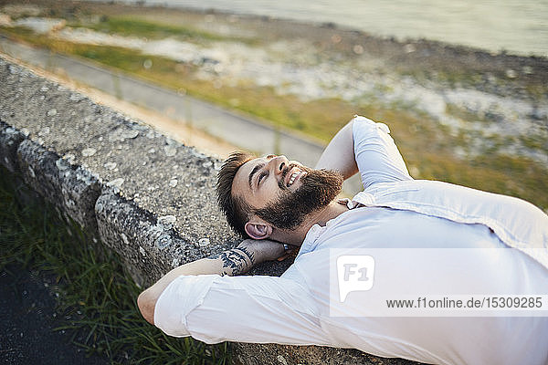 Mann mit Bart auf einer Mauer am Flussufer liegend