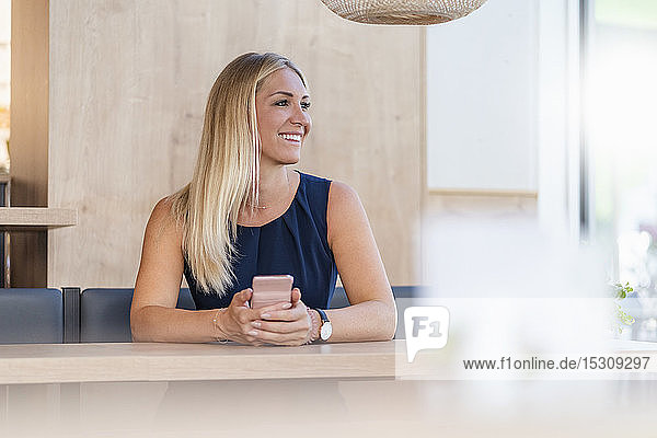 Porträt einer lächelnden blonden Geschäftsfrau mit Smartphone  die in einem Café wartet