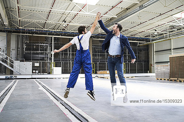Excited businessman and worker jumping and high fiving in a factory