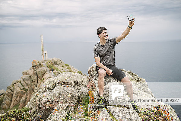 Trailrunner sitzt auf einem Felsen in der Küstenlandschaft und nimmt ein Selfie  Ferrol  Spanien