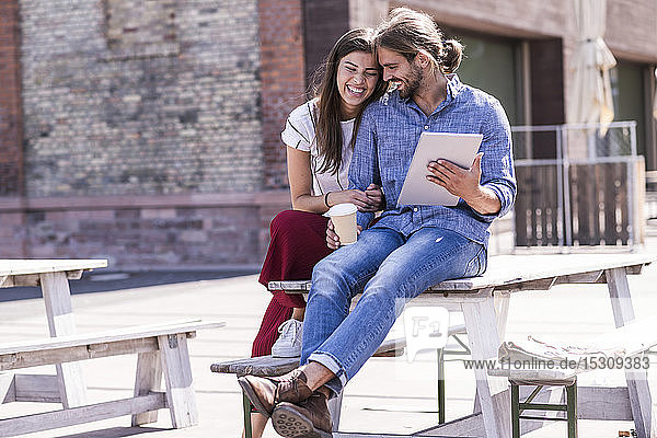 Happy young couple sitting on table in a beer garden with tablet