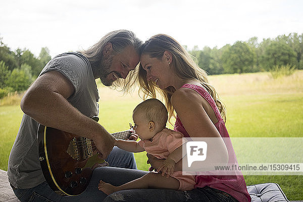 Father  mother and baby girl sitting outdoors with guitar