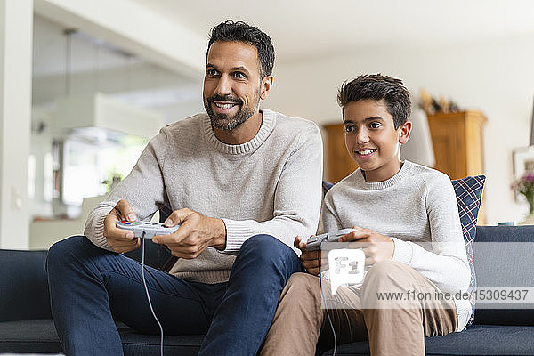 Glücklicher Vater und Sohn spielen Videospiel auf der Couch im Wohnzimmer