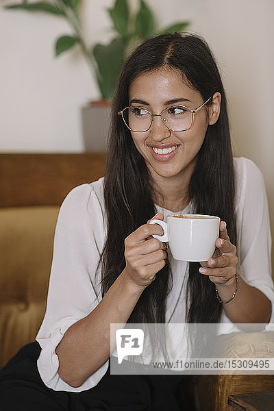 Lächelnde junge Frau mit Tasse Kaffee im Sessel eines Cafés sitzend