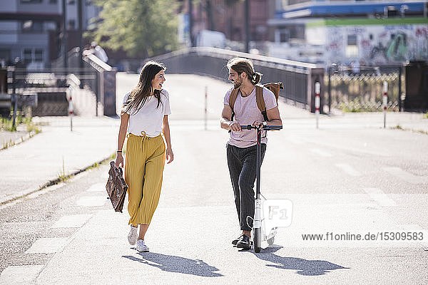 Junges Paar mit Elektroroller läuft und spricht auf der Straße