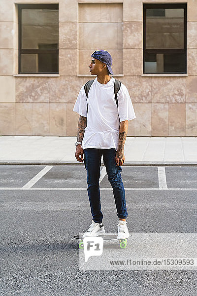 Tattooed young man standing on skateboard looking at distance