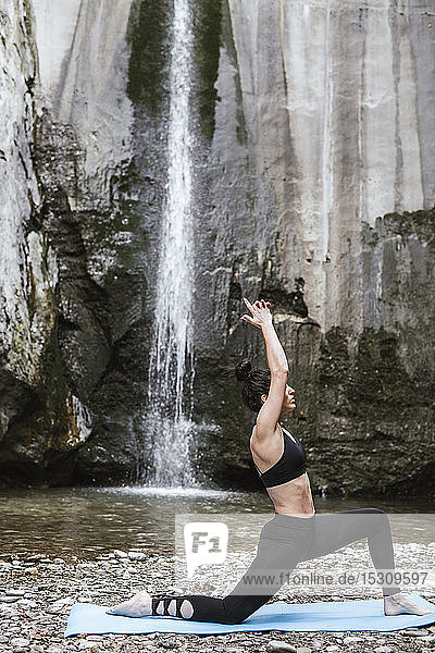 Frau praktiziert Yoga am Wasserfall  Krieger-Pose