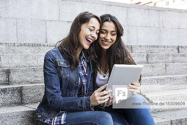 Glückliche junge Frauen schauen Tablet an  die in Madrid  Spanien  gemeinsam auf Stufen sitzen