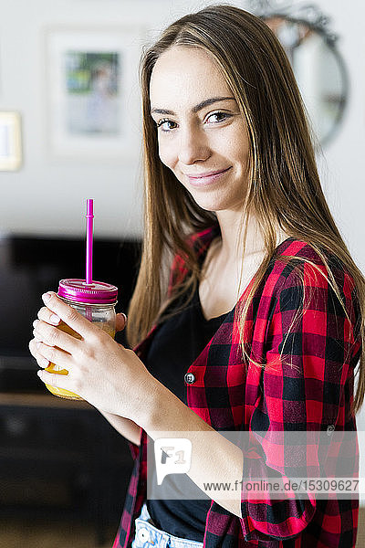 Porträt einer lächelnden jungen Frau mit einem gesunden Getränk zu Hause