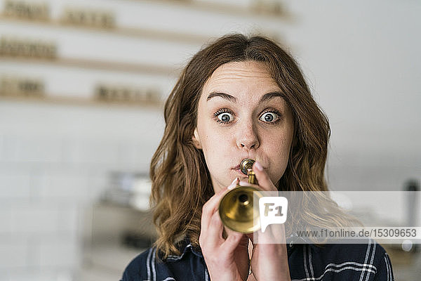 Junge Frau bläst in ihrem Café Spielzeugtrompete