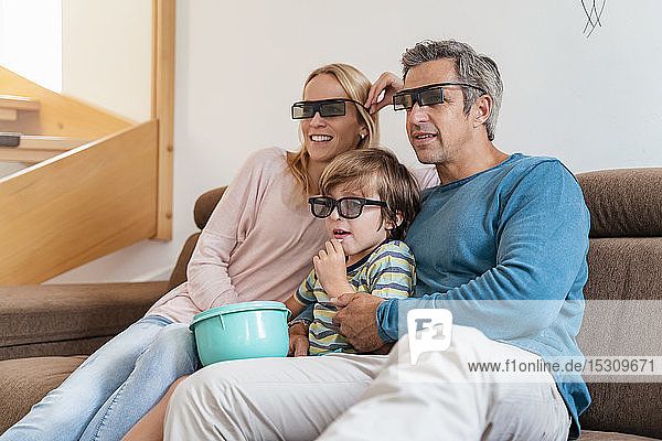 Vater  Mutter und Sohn tragen zu Hause auf der Couch eine 3D-Brille und sehen fern