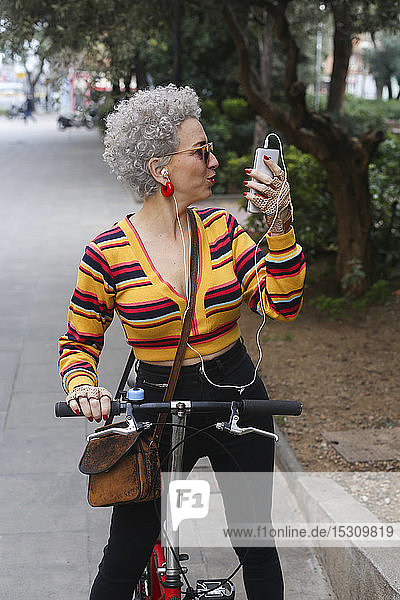 Fashionable mature woman with bicycle using smartphone