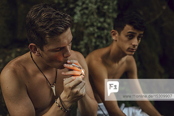 Zwei barbusige Freunde rauchen in der Natur einen Joint Marihuana