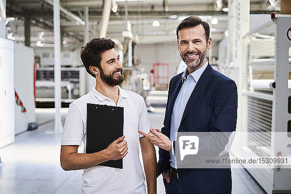 Porträt eines lächelnden Geschäftsmannes und Angestellten mit Klemmbrett in einer Fabrik