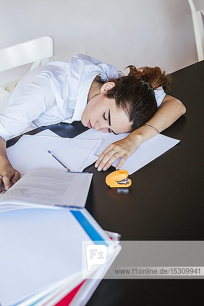 Exhausted female student lying on desk at home with documents