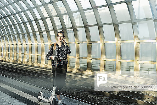 Junge Frau mit Elektroroller auf dem Handy am Bahnhof