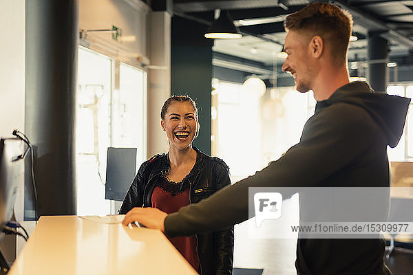 Lachende junge Frau im Gespräch mit dem Trainer an der Rezeption einer Sporthalle