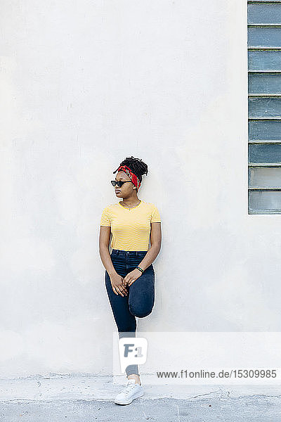 Young woman wearing hair-band and sunglasses leaning against white wall