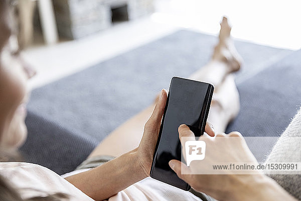 Nahaufnahme einer entspannten Frau  die zu Hause auf der Couch ein Smartphone benutzt