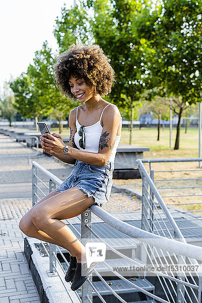 Porträt einer tätowierten jungen Frau  die sich im Sommer mit einem Smartphone selbstständig macht
