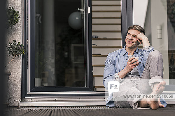 Lächelnder Mann macht eine Pause  trinkt Kaffee vor seinem Haus