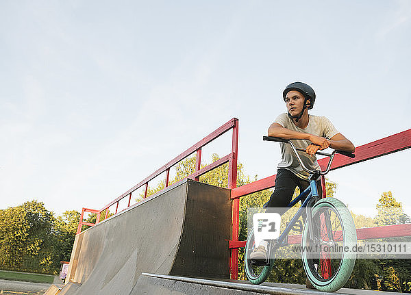 Junger Mann mit BMX-Rad im Skatepark bei einer Pause