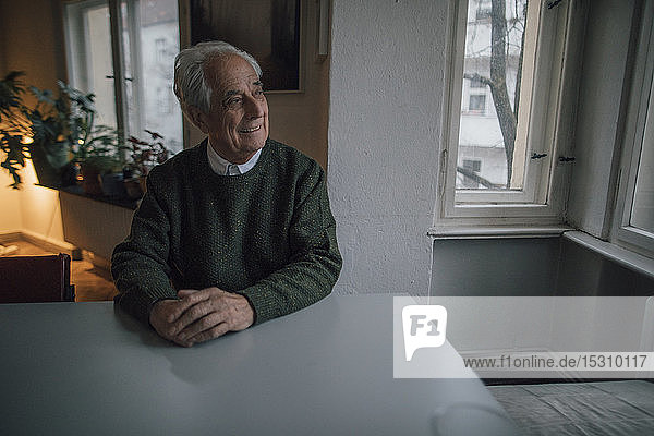 Lächelnder älterer Mann sitzt zu Hause am Tisch