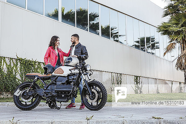 Couple with motorcycle helmets standing beside motorbike