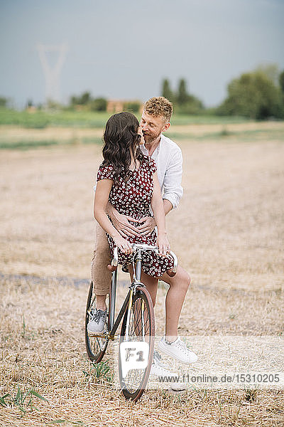 Küssendes Paar mit handgefertigtem Rennrad auf Stoppelfeld