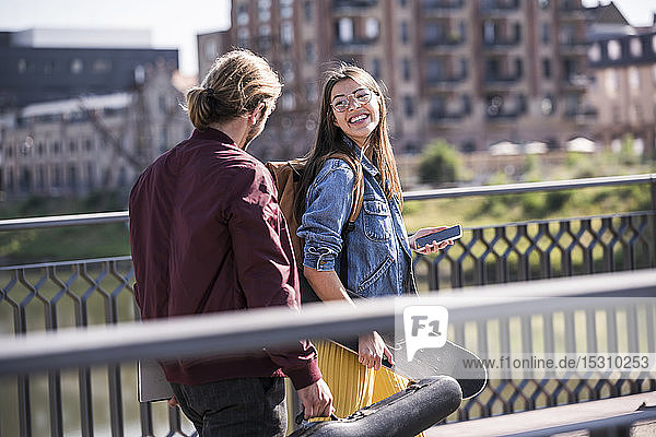 Glückliches junges Paar mit Skateboard auf einer Brücke