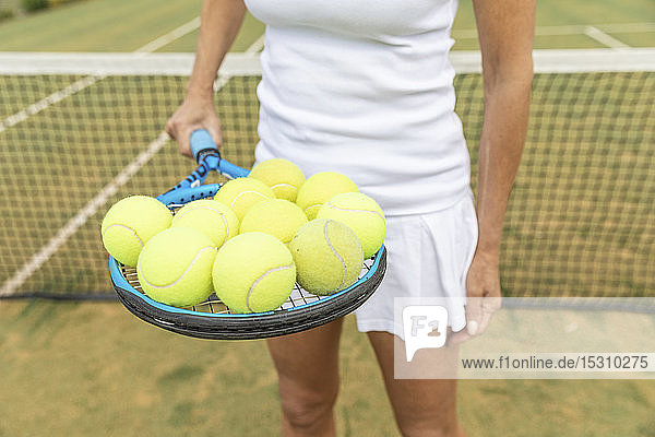 Tennisspielerin  die einen Tennisschläger mit Bällen auf dem Rasenplatz hält