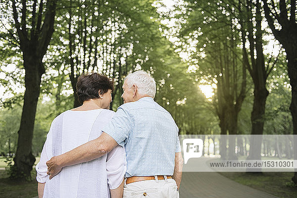 Rückenansicht eines älteren Ehepaares beim abendlichen Spaziergang in einem Park