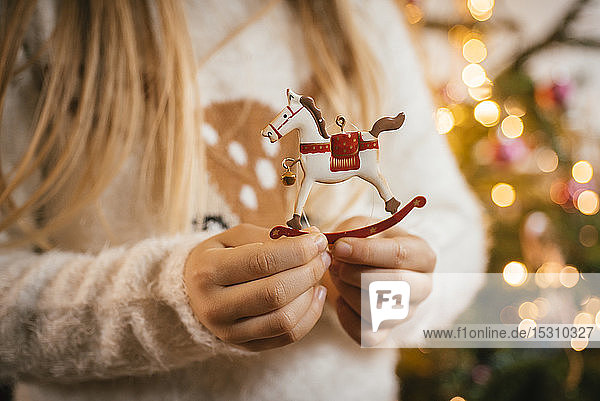 Den Weihnachtsbaum schmücken  Mädchen hält ein Schaukelpferd aus Ziermetall