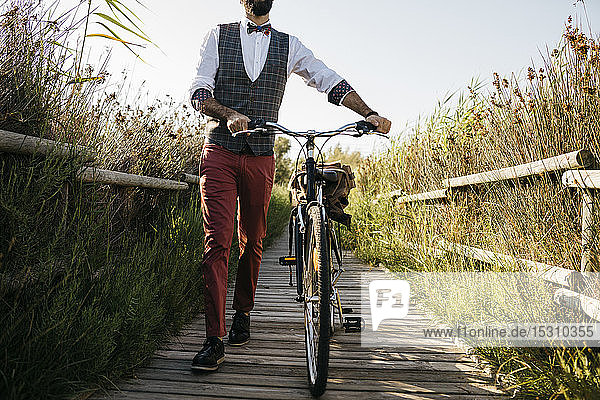 Gut gekleideter Mann  der nach der Arbeit mit dem Fahrrad auf einem Holzsteg auf dem Land unterwegs ist