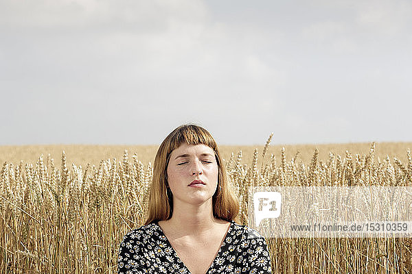 Bildnis einer jungen Frau mit geschlossenen Augen  die sich vor einem Kornfeld entspannt
