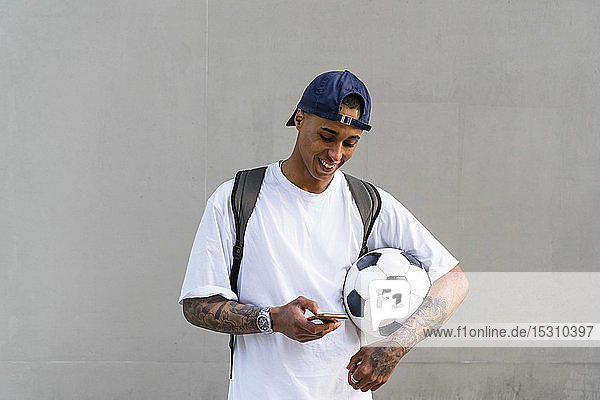 Tattooed young man with football alooking at smartphone