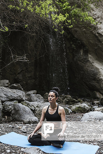 Frau praktiziert Yoga und meditiert am Wasserfall