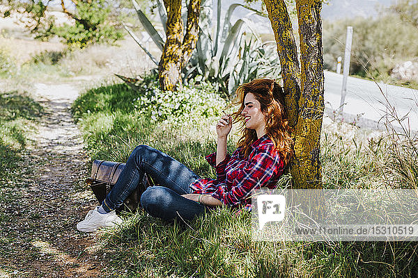 Redheaded woman having cigarette break under a tree