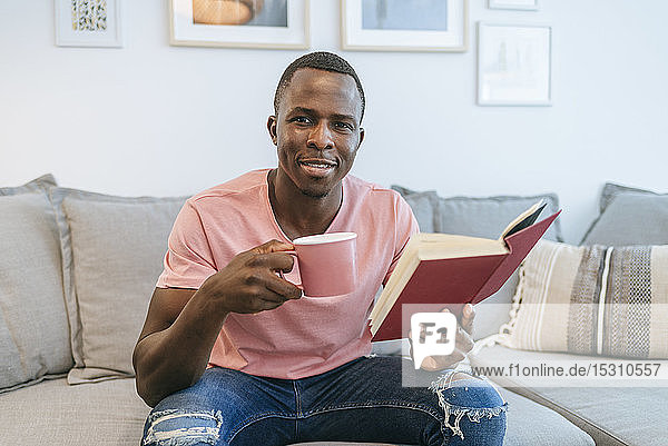 Porträt eines jungen Mannes mit Buch und Tasse Kaffee zu Hause