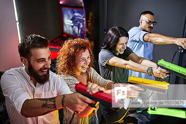 Happy friends playing and shooting with pistols in an amusement arcade