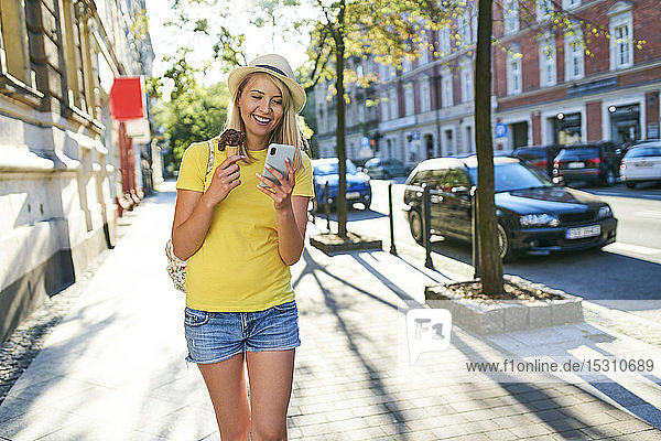Lächelnde junge Frau mit Eiscreme und Handy in der Stadt