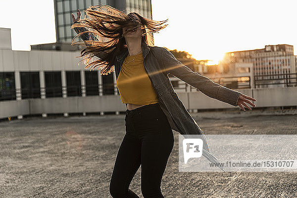Fröhliche junge Frau tanzt bei Sonnenuntergang auf dem Parkdeck