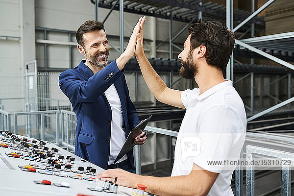 Glücklicher Geschäftsmann und Angestellter mit einem High-Five-High-Five an der Schalttafel in einer Fabrik