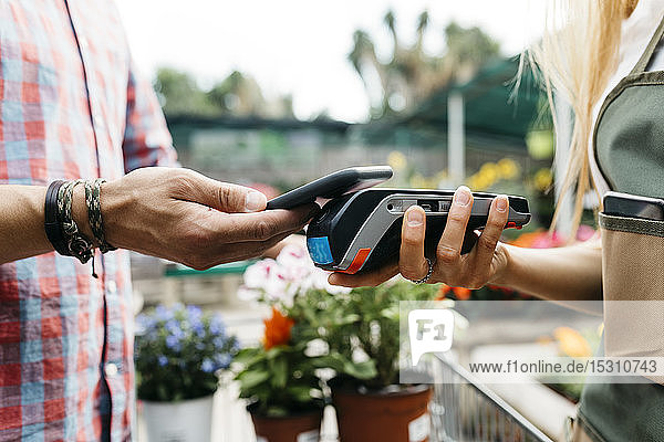 Nahaufnahme eines Kunden  der in einem Gartencenter mit einem Smartphone bezahlt