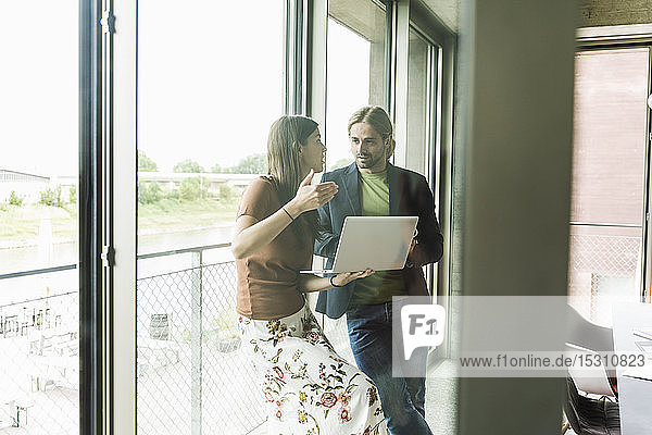 Junge Geschäftsfrau und Geschäftsmann mit Laptop am Fenster im Büro