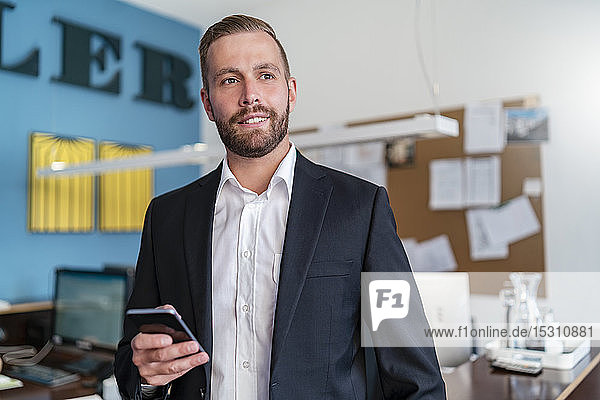Lächelnder Geschäftsmann mit Handy im Büro
