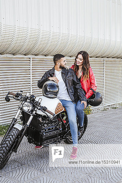 Glückliches Paar mit Motorradhelmen auf Motorrad sitzend